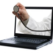 doctor's hand holding stethoscope coming out of computer screen representing telemedicine