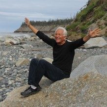 Older gentleman sitting on rocky beach with arms thrown out