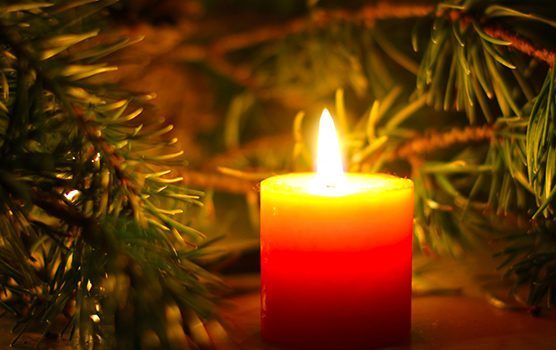 A lit candle surrounded by a fir tree branch