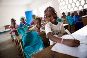 young children sitting at school desks with their backpacks from UNICEF next to them