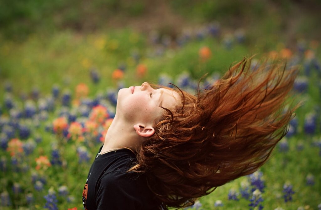 Girl with Red Hair Flipping Her Hair over Head With Her Eyes Closed in a Field of Flowers