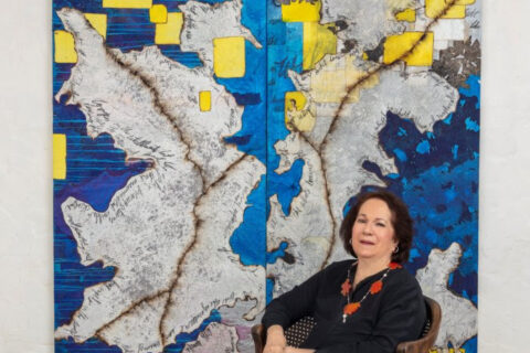 Mira Lehr posing in front of blue, yellow, and grey artwork